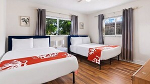 Quarto de hotel com duas camas, ventilador de teto e janelas com cortinas.