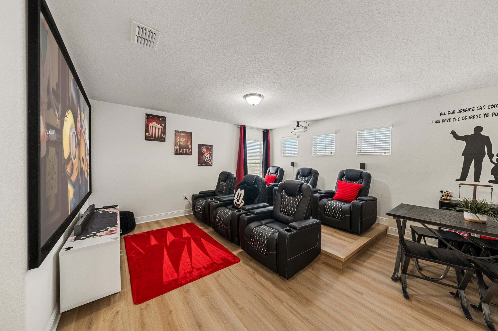 Uma sala de estar com televisão de tela plana, poltronas reclináveis, um tapete vermelho e uma parede com decoração de filmes.