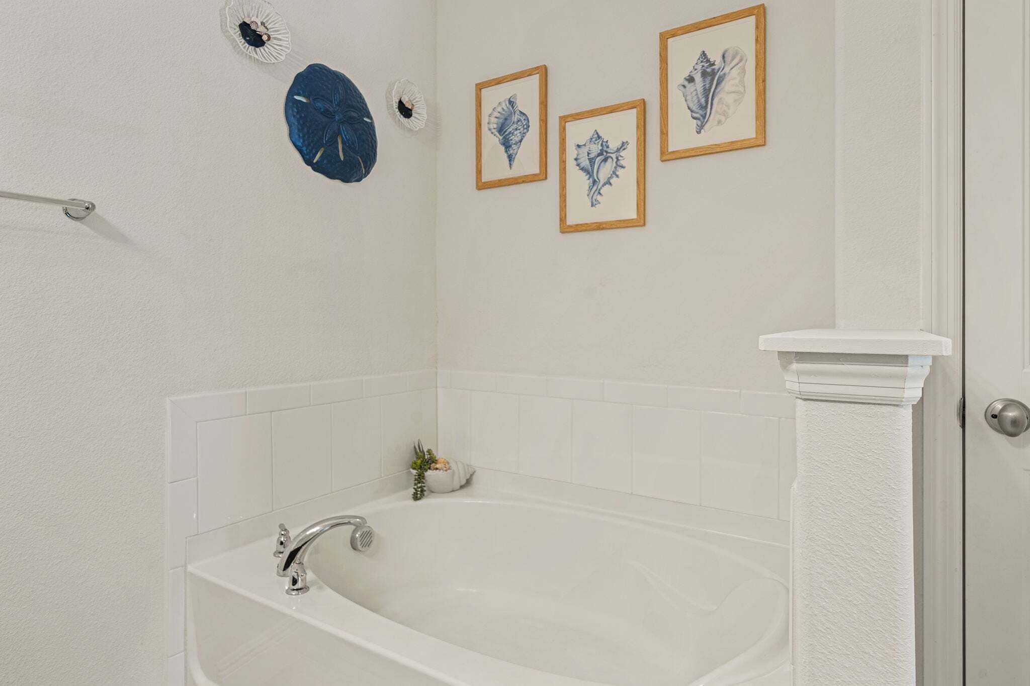 A bathroom with a bathtub, white tiles, a towel rack, and framed pictures on the wall.