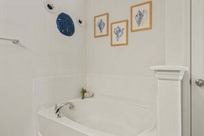 Ein Badezimmer mit einer Badewanne, weißen Fliesen, einem Handtuchhalter und gerahmten Bildern an der Wand.