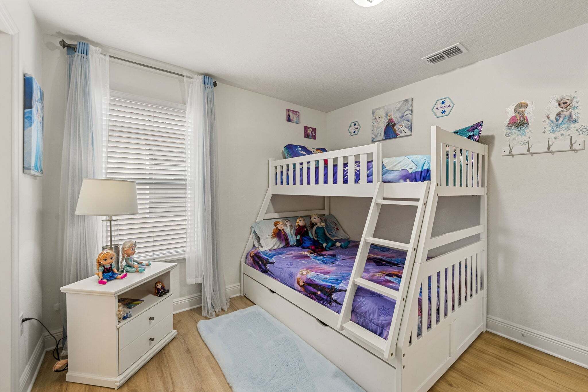 A child's bedroom with bunk beds, a desk, and a window with curtains.