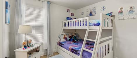 Een kinderkamer met stapelbedden, een bureau en een raam met gordijnen.