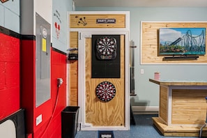 A darts room with two dartboards, a wooden sign above the door, a wall-mounted TV, and a trash bin. - Basketball Arcade, Pool Table, Darts, Giant ConnectFour, Theater: Makin Memories (Davenport)