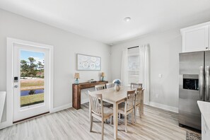 Eine moderne Küche mit Essbereich, einem Kühlschrank und Blick auf einen Garten durch eine Glastür.