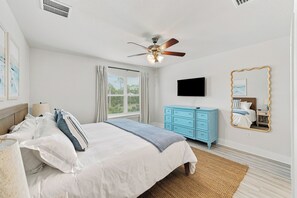 Une chambre à coucher avec un lit, un ventilateur de plafond, une télévision, une commode et un miroir.