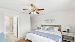 Une chambre à coucher avec un lit, deux tables de chevet, un ventilateur de plafond et des œuvres d’art accrochées au mur.