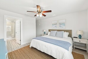 A bedroom with a bed, two bedside tables, a ceiling fan, and artwork on the wall. - Brand-New 4-Bedroom Coastal Escape in WindMark Beach (Port St. Joe)