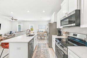 A modern kitchen with white cabinetry, a stainless steel refrigerator, a microwave, and a stove. - Brand-New 4-Bedroom Coastal Escape in WindMark Beach (Port St. Joe)