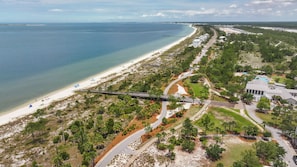 An aerial view of a coastal area with a beach, a road, and buildings. - Brand-New 4-Bedroom Coastal Escape in WindMark Beach (Port St. Joe)