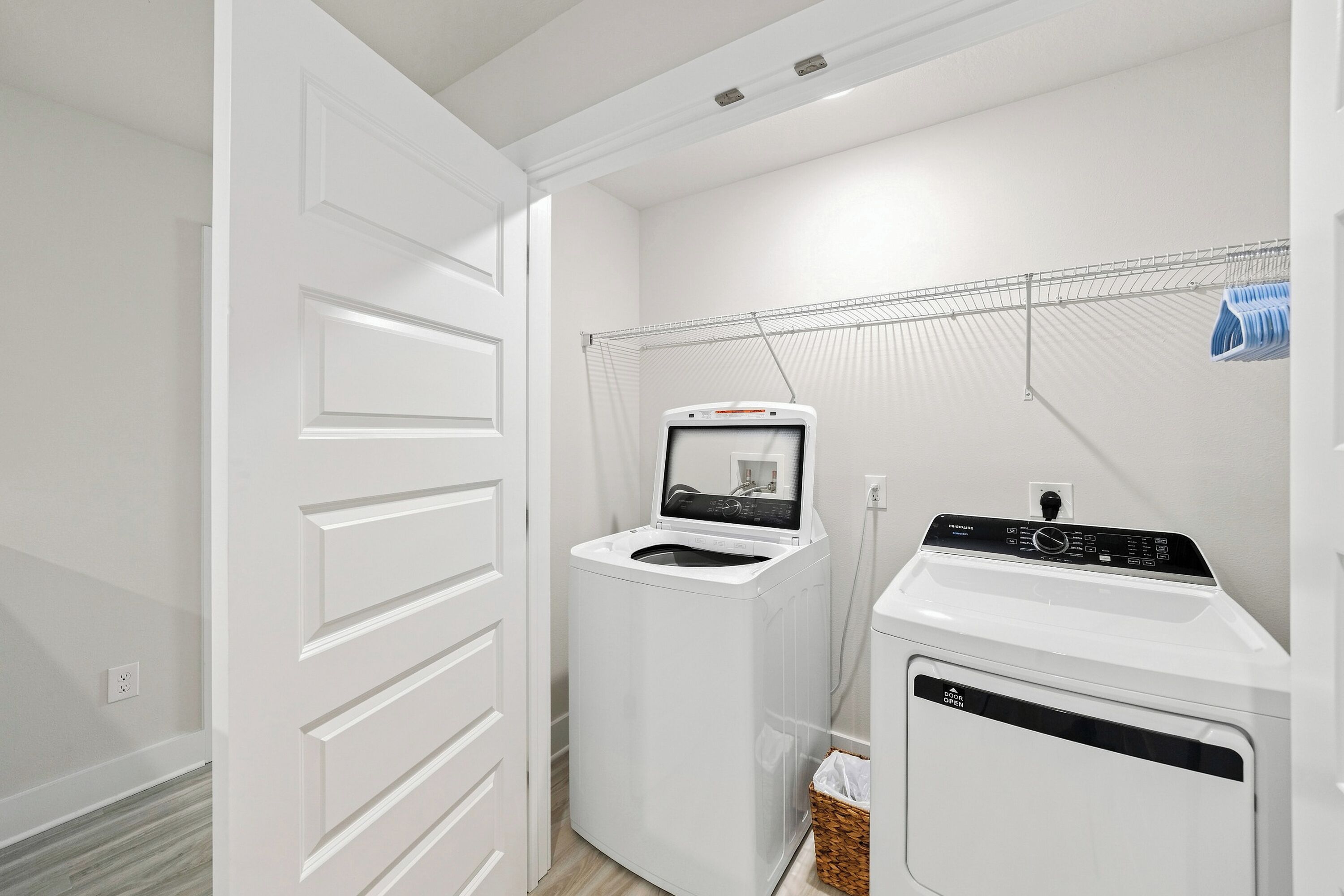 A laundry room with a front-loading washer and dryer, a drying rack, and a basket.