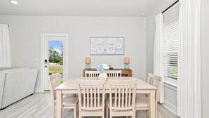 Un coin repas avec une table et des chaises, un tableau accroché au mur et une vue à travers la porte.
