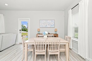 A dining area with a table and chairs, a painting on the wall, and a view through the door. - Brand-New 4-Bedroom Coastal Escape in WindMark Beach (Port St. Joe)