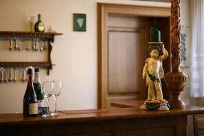 A bar area with a wine bottle, glasses, and a decorative statue on a wooden counter. - Glocke (Rothenburg ob der Tauber)