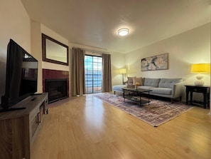 A living room with a television, sofa, coffee table, fireplace, and a view through a glass door. - 2 Bedroom Apt 5 minutes from Rodeo Dr Walk to Restaurants and Markets (Beverly Hills)