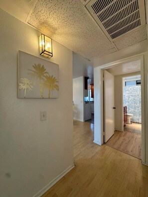 Un pasillo con una lámpara, una puerta que da a un baño y una cocina visible a través de otra puerta abierta.