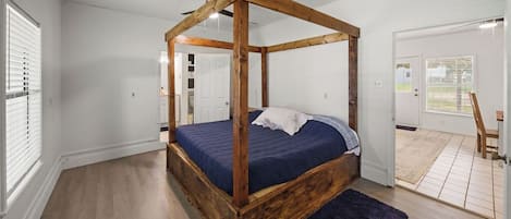 Un dormitorio con cama con dosel, suelo de madera y vistas al exterior a través de una puerta.