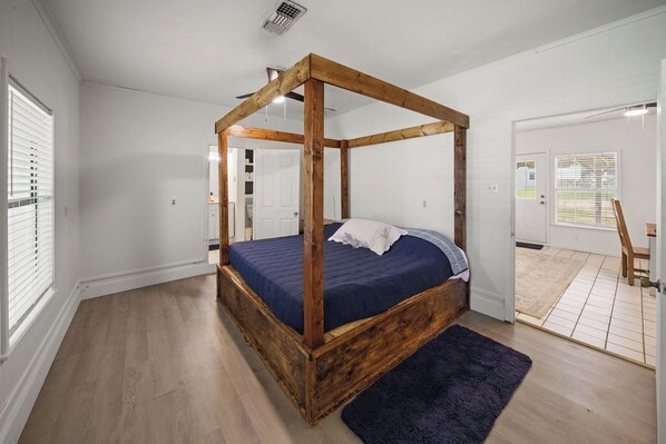 A bedroom with a four-poster bed, wooden flooring, and a view of the outside through a door.