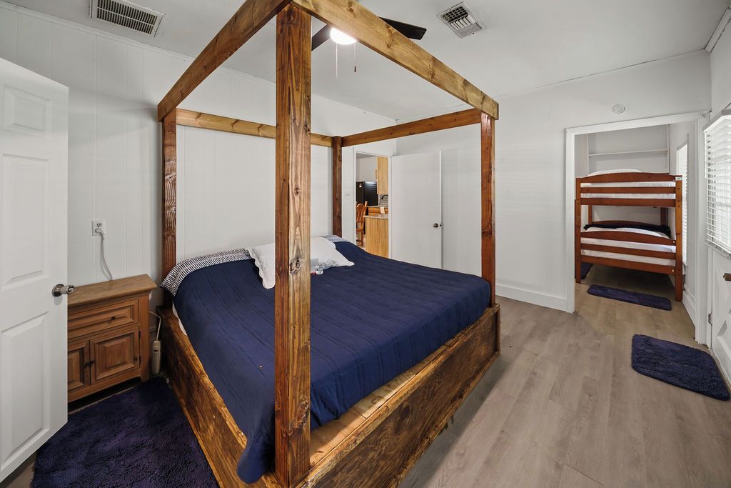 A four-poster bed with a dark blue bedspread, a wooden headboard, and a wooden floor.
