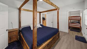 A four-poster bed with a dark blue bedspread, a wooden headboard, and a wooden floor.