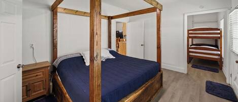 A four-poster bed with a dark blue bedspread, a wooden headboard, and a wooden floor.