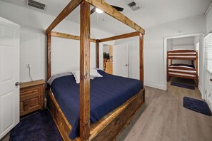A four-poster bed with a dark blue bedspread, a wooden headboard, and a wooden floor.