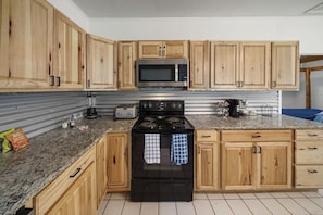 A kitchen with wooden cabinets, a stainless steel microwave, a black stove, and granite countertops.