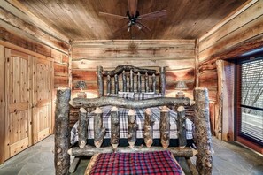 A log cabin interior with a bed featuring a rustic log headboard, a ceiling fan, and a window with blinds. - Rustic Pigeon Forge Cabin with Spacious Living and Dining for Group Getaways (Pigeon Forge)