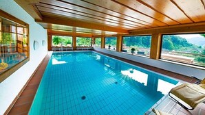 Une piscine intérieure dotée de poutres en bois au plafond, de grandes fenêtres et offrant une vue sur la verdure environnante.