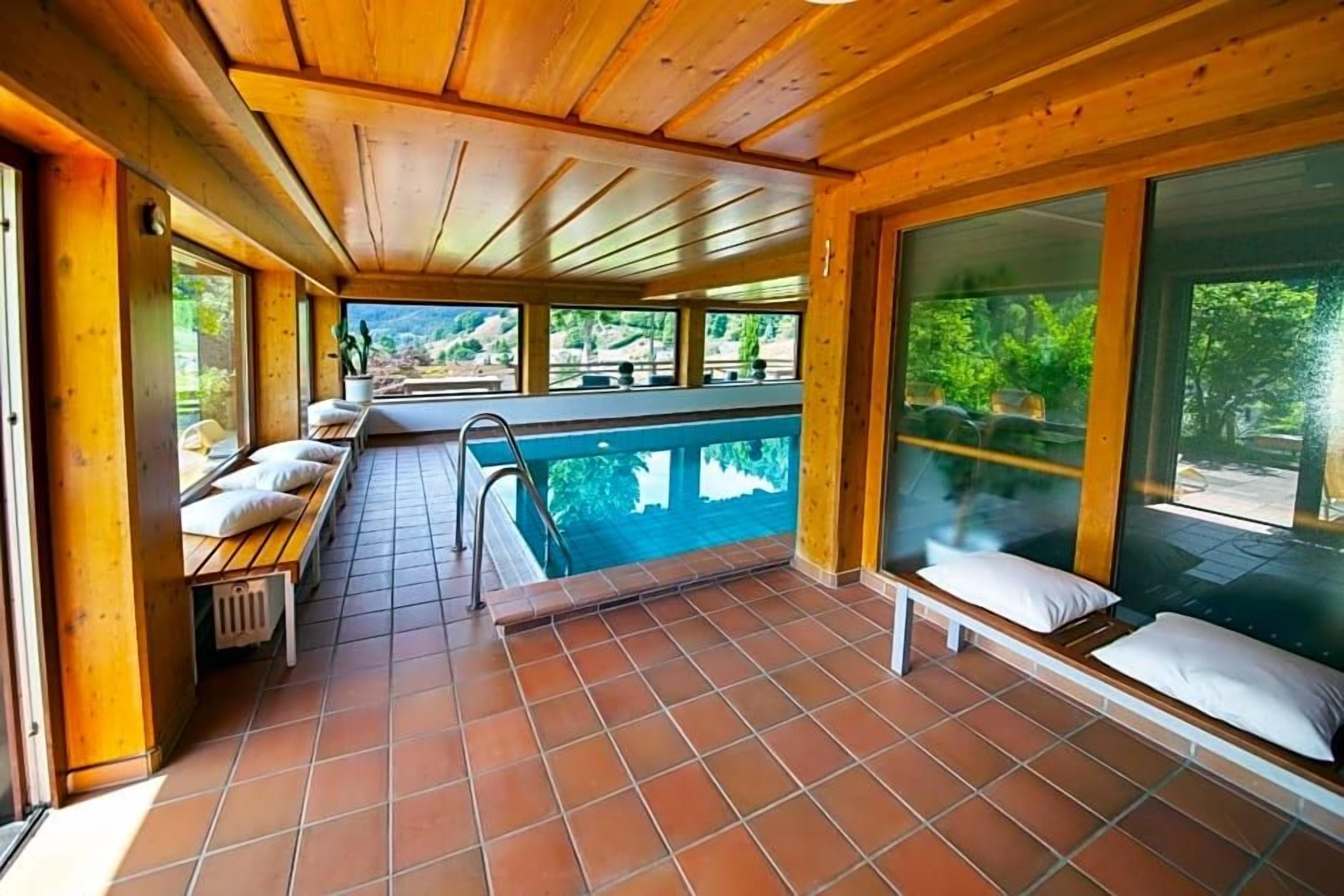 A wooden interior with a pool, benches, and large windows.
