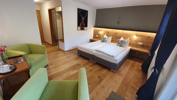 Une chambre d’hôtel avec un lit, un fauteuil vert, une tête de lit en bois et un tableau accroché au mur.
