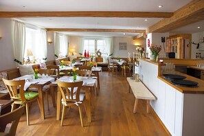 A spacious dining area with wooden tables and chairs, a bar area with a counter, and large windows allowing natural light. - Landhaus Langeck (Münstertal)