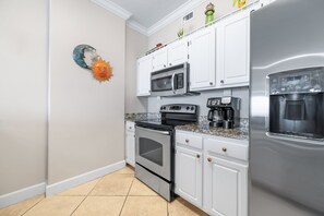A kitchen with white cabinets, a stainless steel refrigerator, a microwave, an oven, and a coffee maker. - Grand Pointe 603 | Beachfront, Pools, Saunas, Hot Tub | My Beach Getaways (Orange Beach)