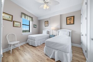 A bedroom with two beds, a window with blinds, a chair, and framed pictures on the walls. - Grand Pointe 603 | Beachfront, Pools, Saunas, Hot Tub | My Beach Getaways (Orange Beach)