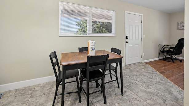 A dining area with a table and chairs, a window with blinds, a door, and a small office chair.