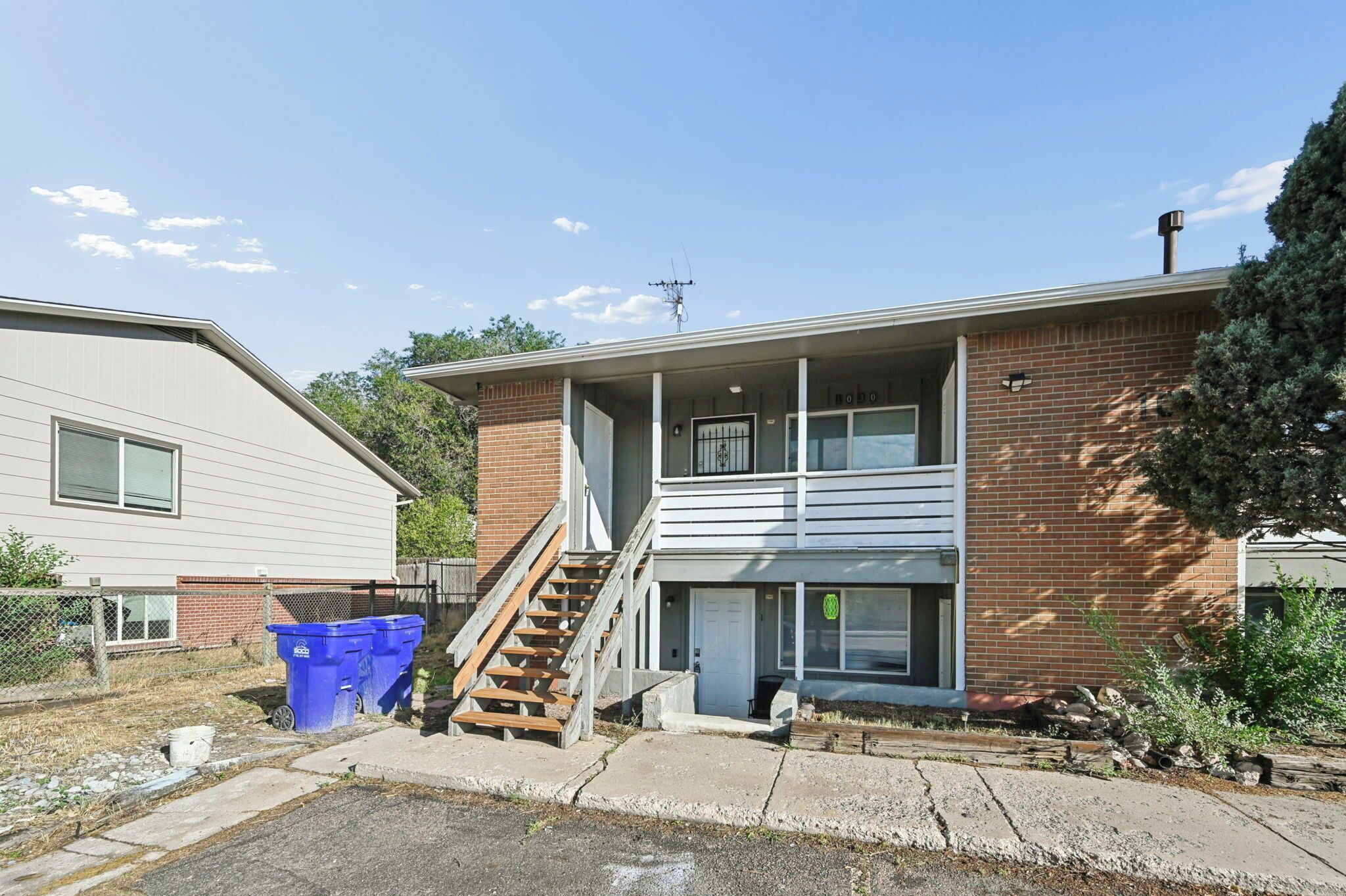 A two-story residential building with a visible staircase leading to the upper floor, a front door, and a small porch area.