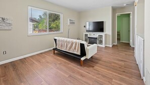 A spacious living room with hardwood flooring, a sofa, a flat-screen TV, and a fireplace.