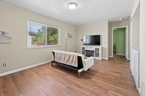 Een ruime woonkamer met houten vloeren, een bank, een flatscreen-tv en een open haard.