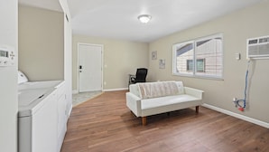 A room with a white sofa, a washing machine, a door, and a window with blinds.