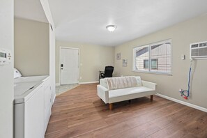 Habitación con sofá blanco, lavadora, puerta y ventana con persianas.