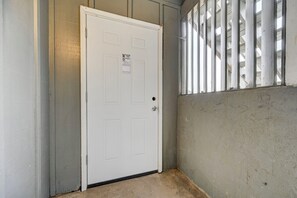 Eine weiße Tür mit einem kleinen Fenster, einem Betonboden und einem Metallgeländer.