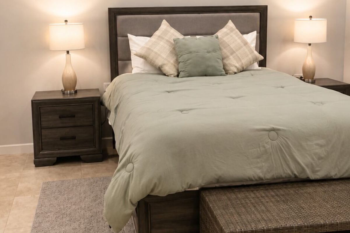 A bedroom with a bed, two bedside tables with lamps, a bench, and a rug.