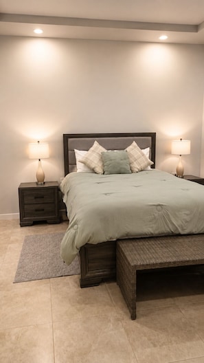 A bedroom with a bed, two bedside tables with lamps, a bench, and a rug.