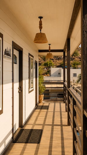 A corridor with doors, a hanging light fixture, a wooden floor, and a view of buildings in the distance. - Cabañas Villa Sierra Privada San Carlos (Ensenada)