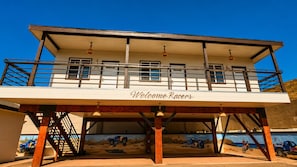 A building with a 'Welcome Racers' sign, a covered area with a mural, and a staircase leading to an upper level. - Cabañas Villa Sierra Privada San Carlos (Ensenada)