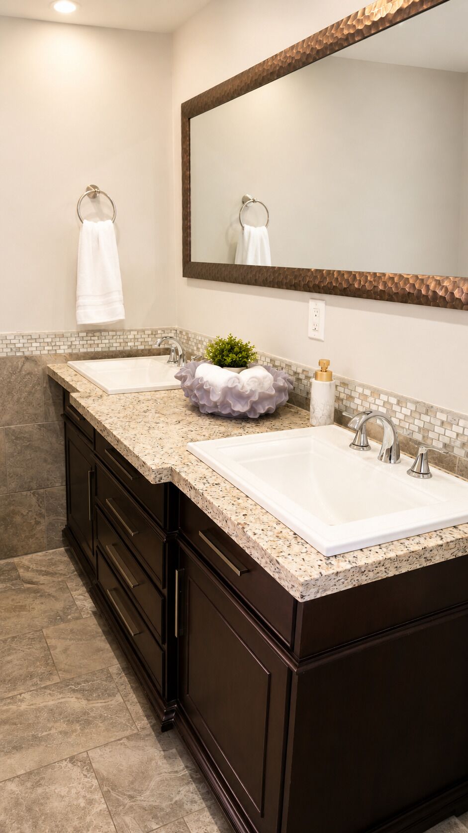 A bathroom with two sinks, dark cabinetry, a large mirror, and a decorative plant.