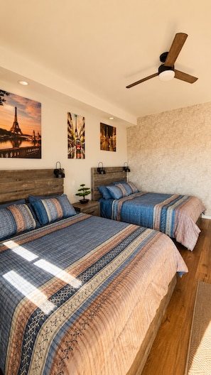 A bedroom with two beds, a ceiling fan, and wall art depicting Parisian scenes. - Cabañas Villa Sierra Privada San Carlos (Ensenada)
