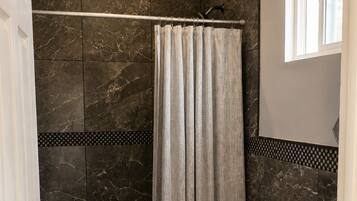 Un baño con inodoro, ducha con cortina y paredes de mármol oscuro.