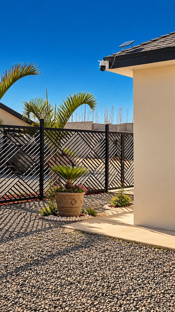 A paved patio area with a decorative fence, a potted plant, and a building with a solar panel. - Cabañas Villa Sierra Privada San Carlos (Ensenada)