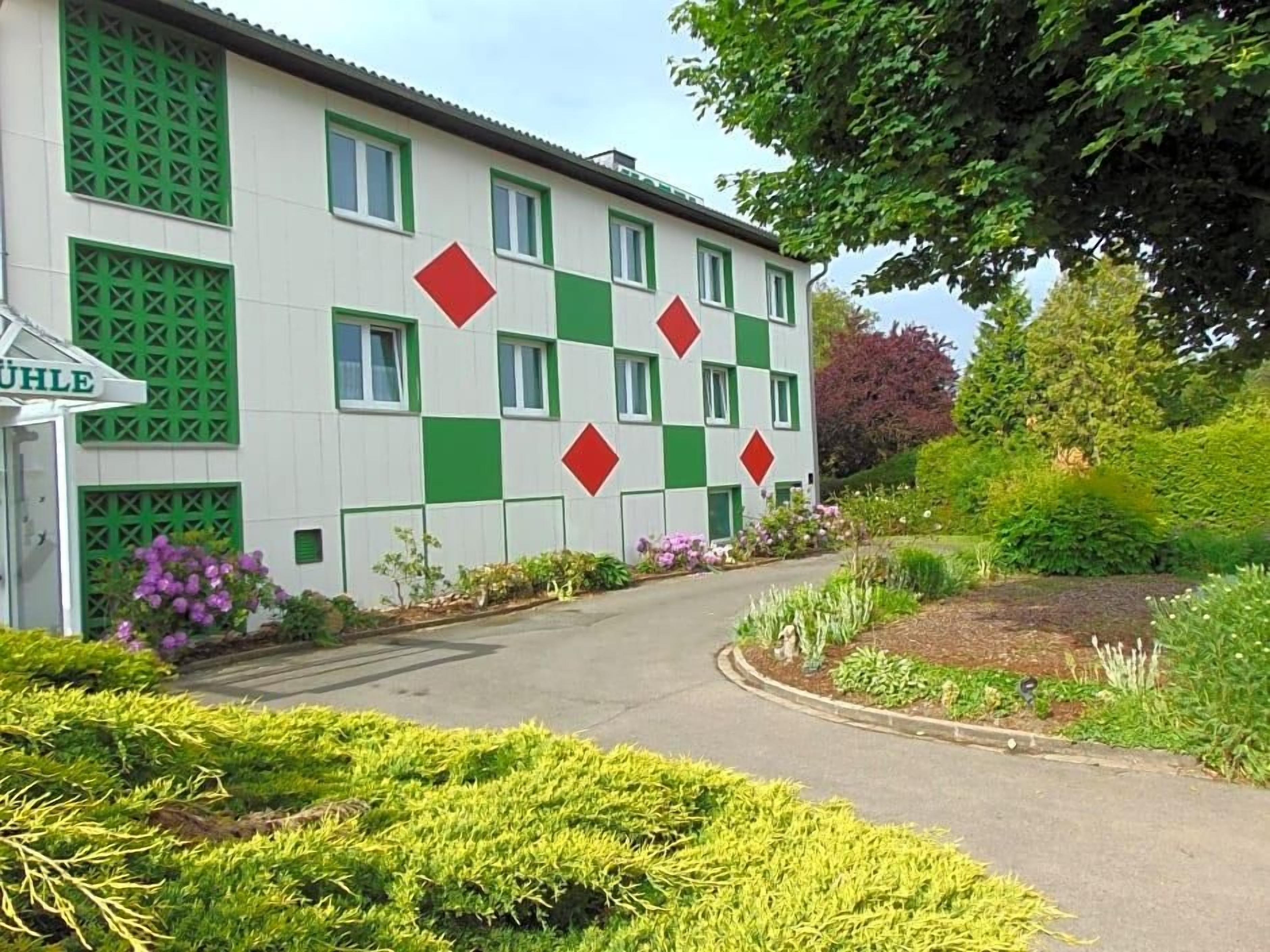 Un bâtiment à la façade à carreaux, une enseigne indiquant « BüLe », et un jardin bien entretenu.