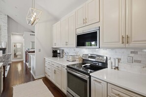 Une cuisine moderne avec des meubles blancs, un four à micro-ondes encastré, une cuisinière en acier inoxydable et un luminaire suspendu.